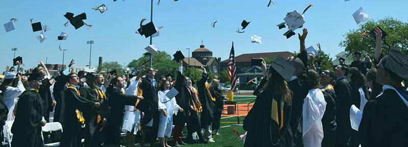 Photo of graduates in gowns throwing their caps into the air