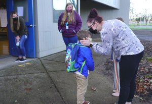 Mom kissing her child good-bye outside the classroom outer door