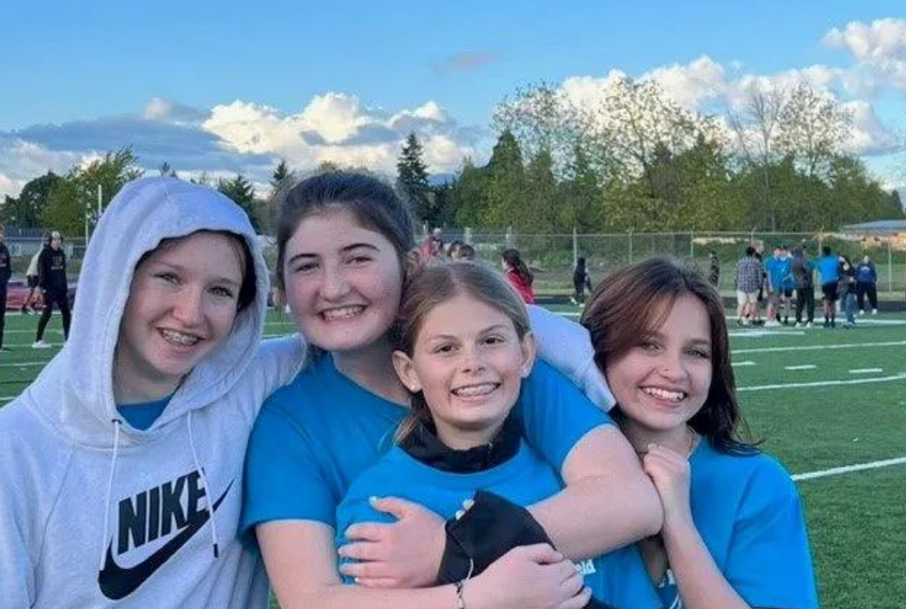 A group of 4 students on a football field smiling at the camera