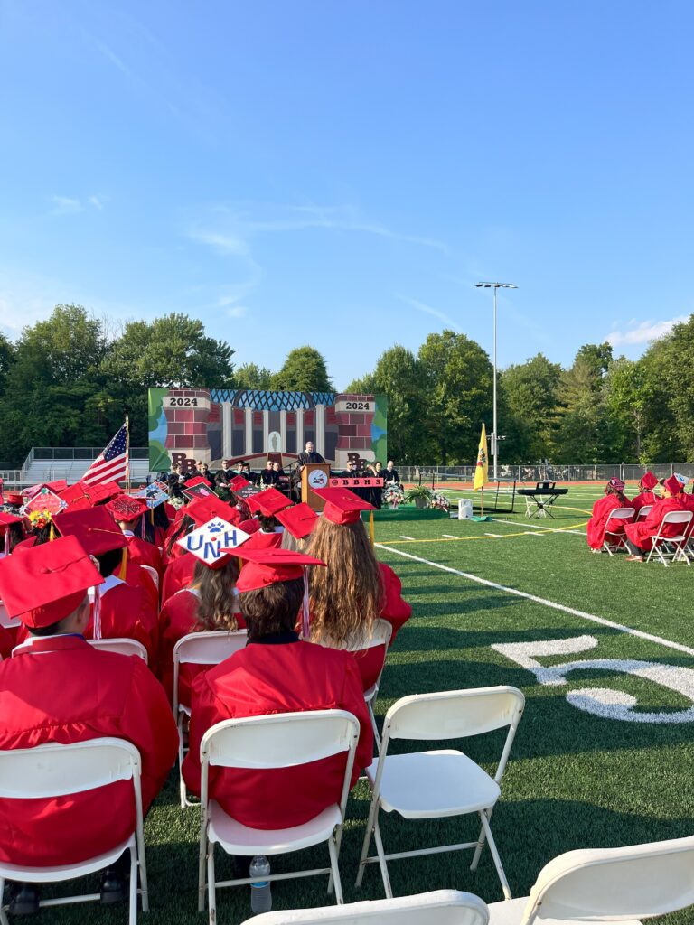 The class of 2024 excitedly sit on the field facing the stage where Principal Edward Smith address the graduates.