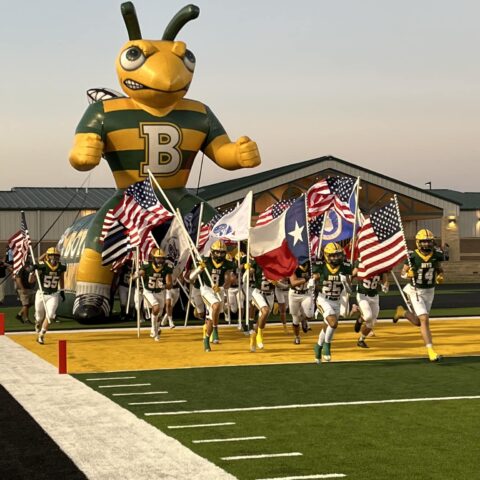 photo of football team running through the inflatable yellowjacket carrying flags