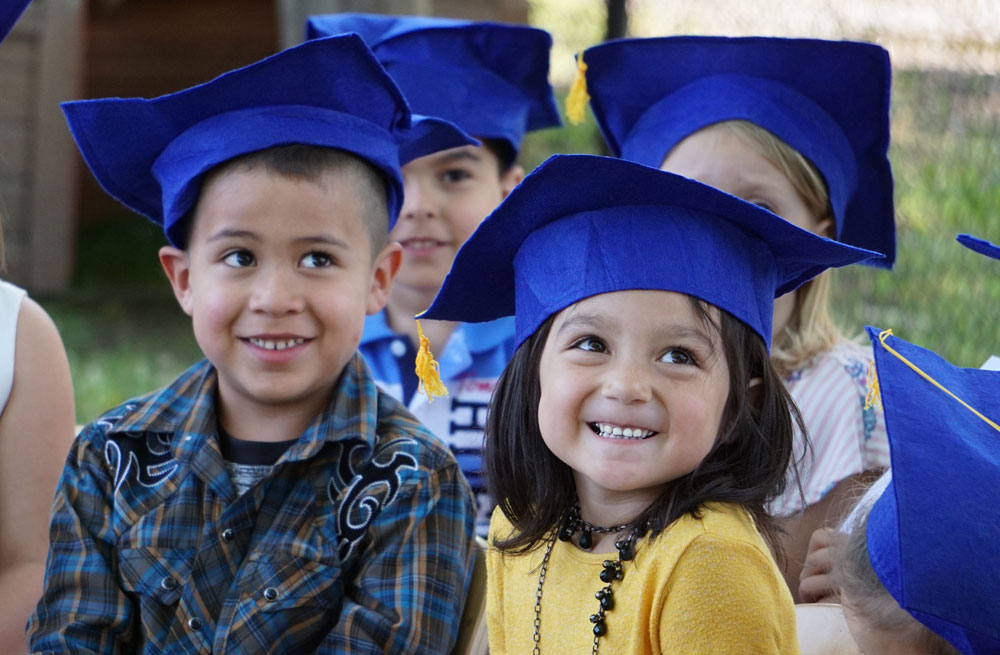 4 preschool students with blue graduation caps on their heads