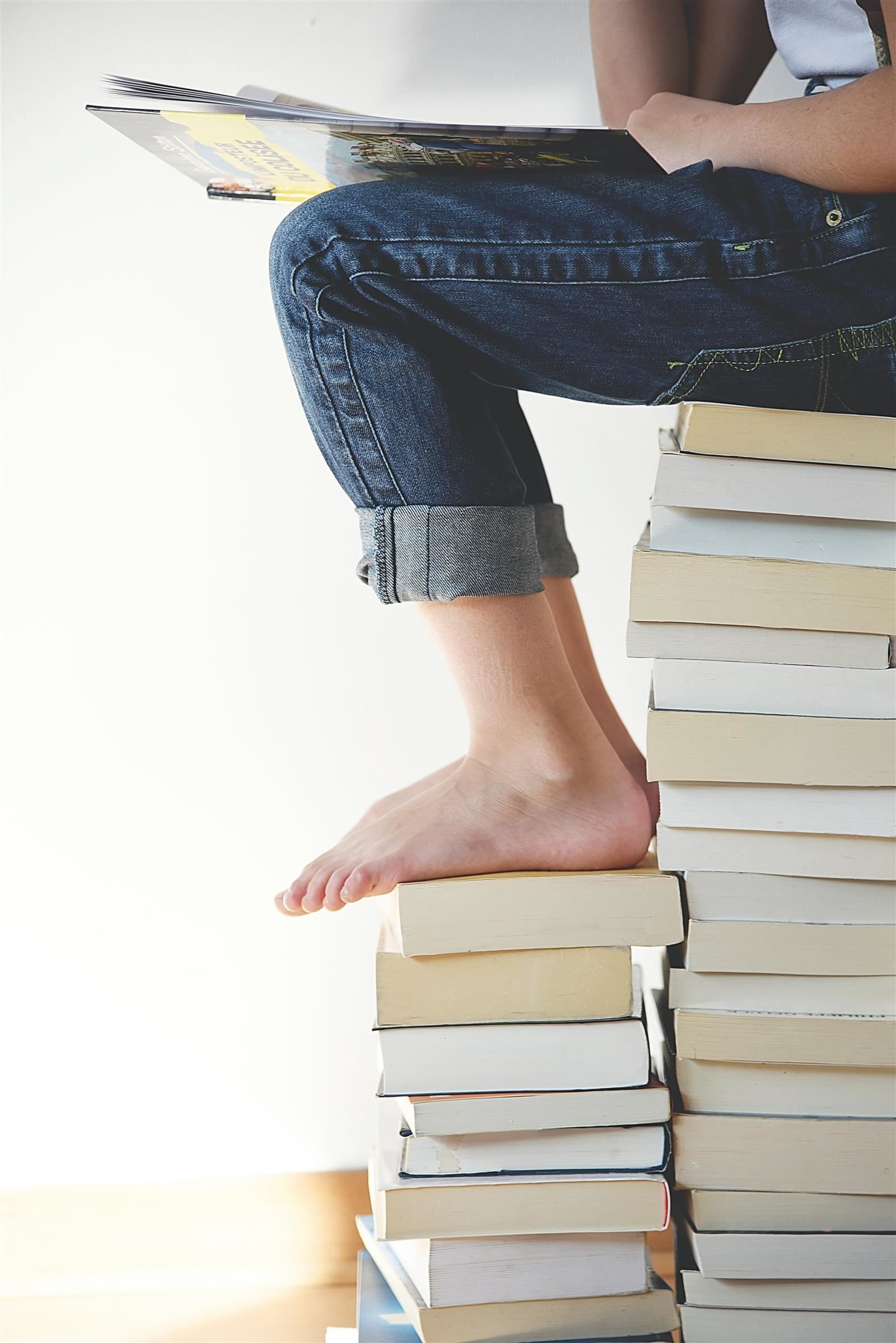 child sitting on a stack of books reading