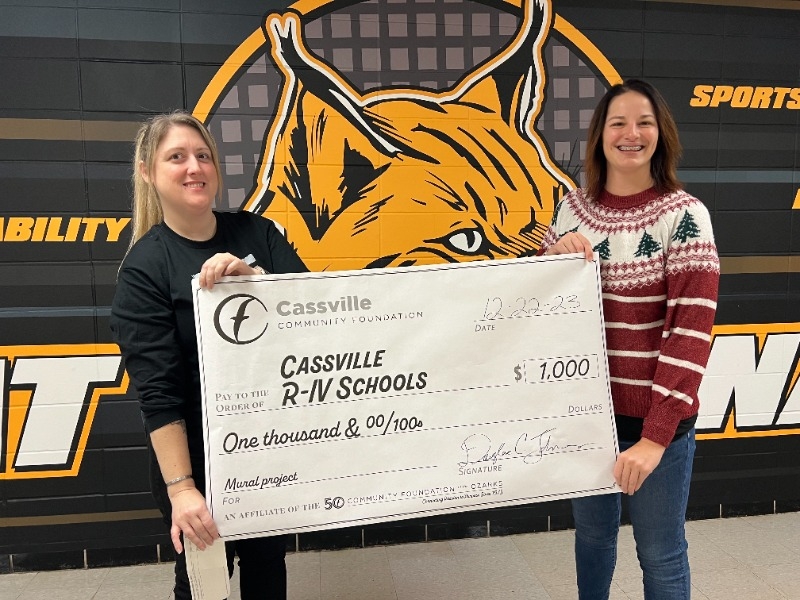 2 women holding a large paper check celebrating a $1,000 donation to the local art club.