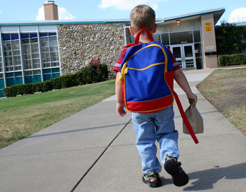 Child walking towards a school holding a lunch bag. 