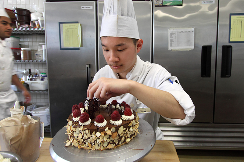 Student decorating a cake in the kitchen.