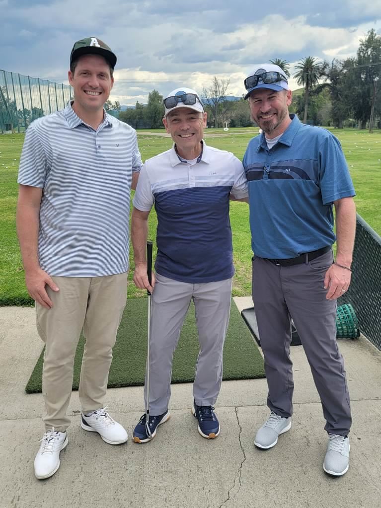 Three golfers posing together with a smile