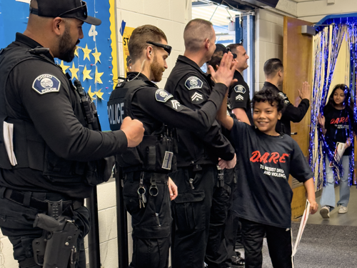 Male D.A.R.E. student high-fiving police officers during graduation.