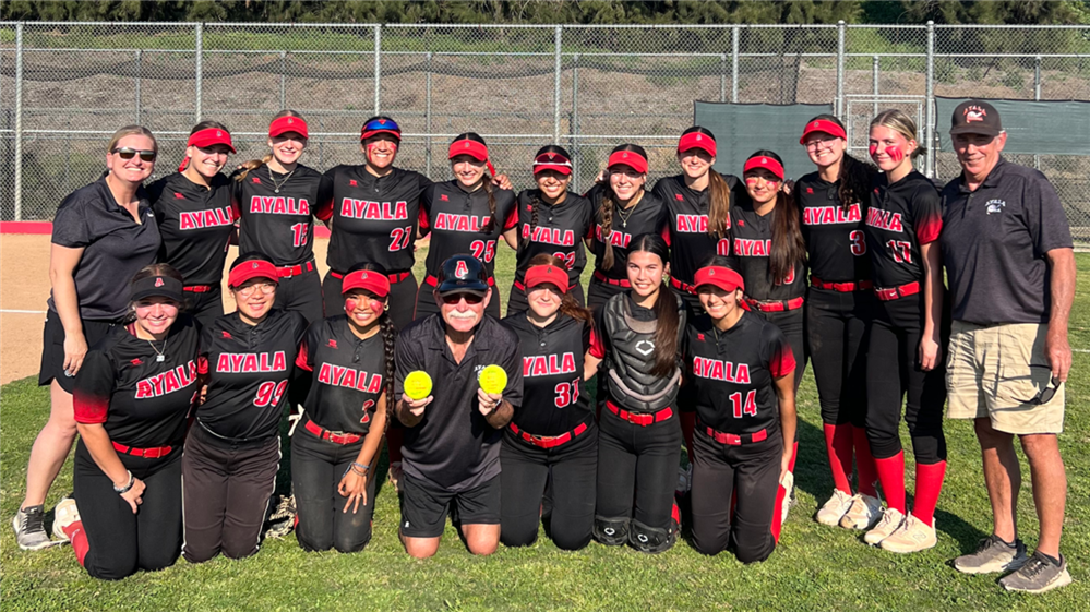  Coach Ameluxen holding two softballs while surrounded by the softball team