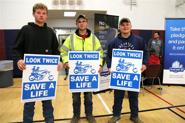 Three students hold "look twice save a life" signs.