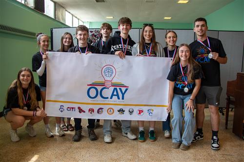 A group of students wearing medals gather around an OCAY League banner.