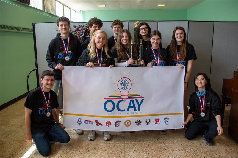  A group of students wearing medals gather around an OCAY League banner.