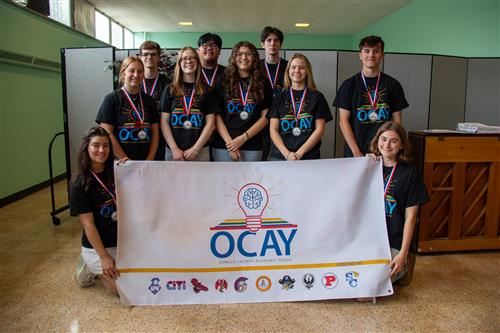 A group of students wearing medals gather around an OCAY League banner.