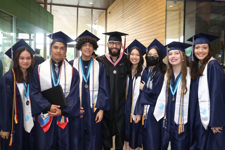 Seven Harrison Prep graduates smiling and posing for post graduation photo with Harrison Prep staff member