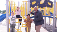 El superintendente Ron Banner posa frente a los juegos del parque infantil con tres estudiantes.
