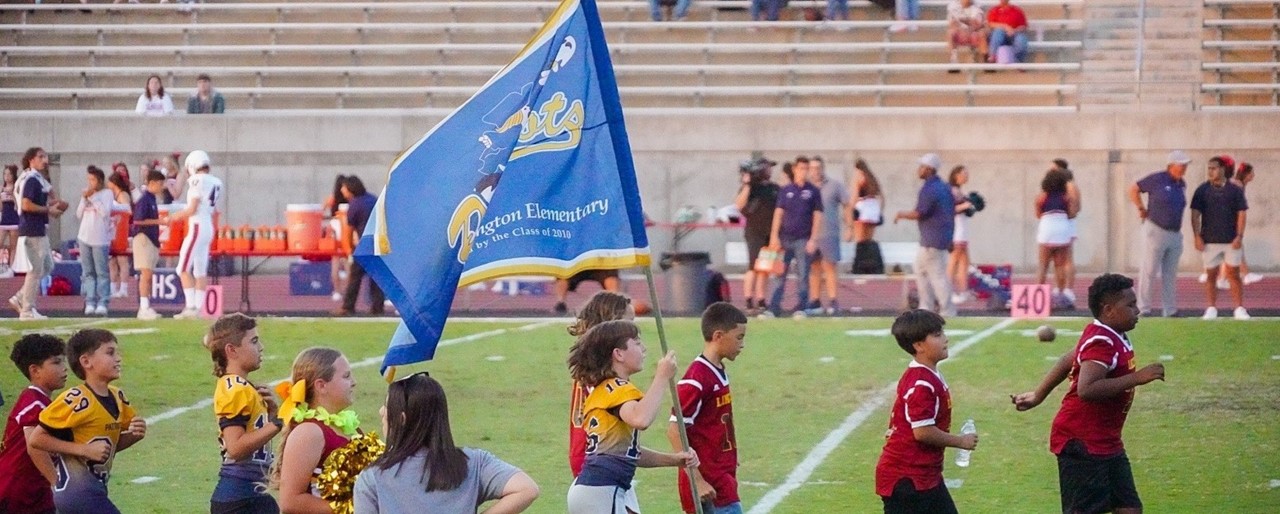 Image of FW football players and cheerleaders carrying the FW school flag at FW School Feeder Night at Buchanan Stadium.