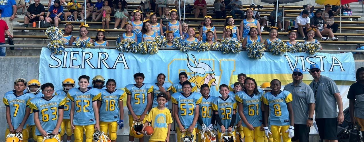 Football and cheerleaders standing in front of a sign