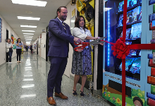 Dr. Cox and Principal Rihn cut ribbon afixed to vending machine.