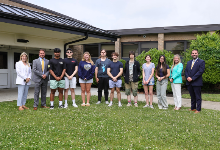 Group of scholarship winners poses outside school's main entrance with principal and district officials.