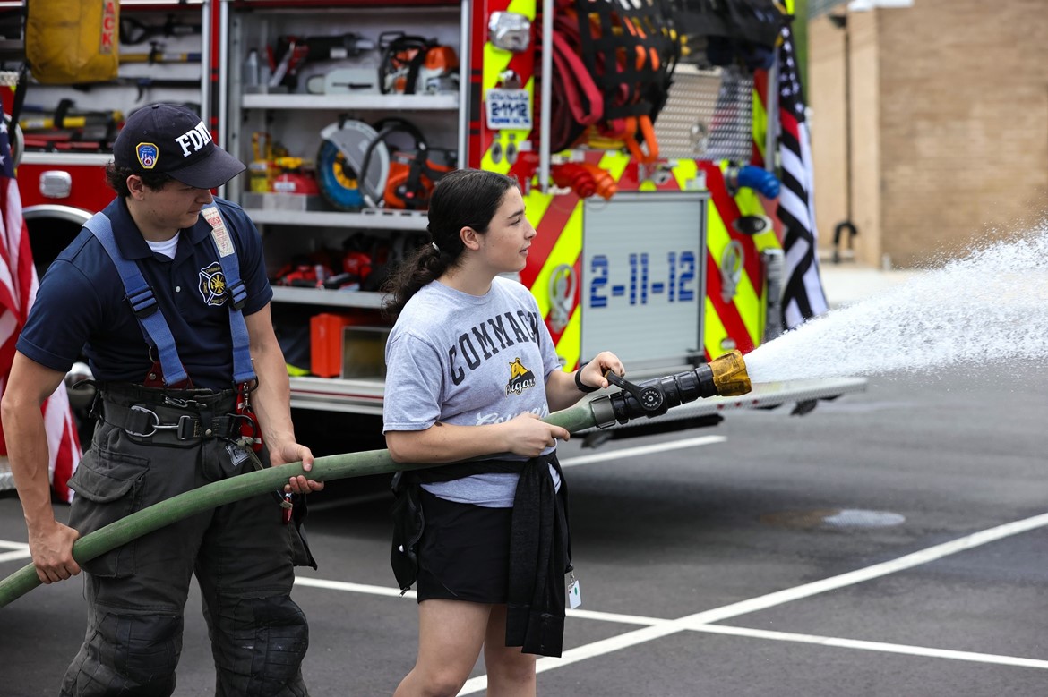 Student holds fire hose with assistance from Commack firefighter during Commack Day exhibition.