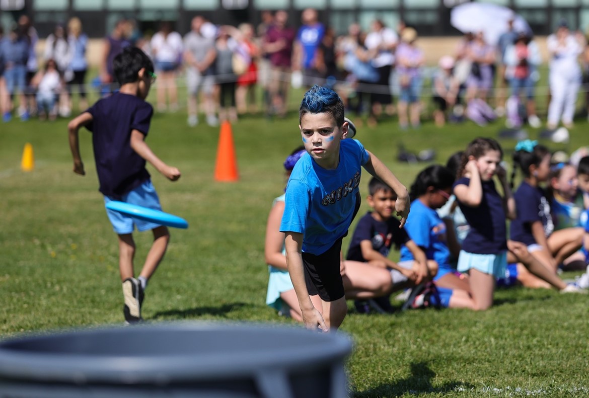 Student on blue team in Burr third grade field day tosses frisbee, aiming for garbage can.