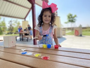 A Compass’ Online Learning Program scholar digs her paint sponge stick into primary colors of paint for an art project. She smiles with hope.