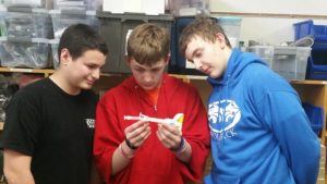 Three students look at a prototype of the experiment they designed.