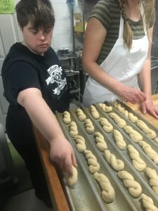 A supported staff member at Reality Kitchen prepares soft pretzel dough for baking.