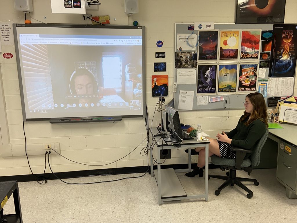 Student appears on screen, second student sits in front of computer