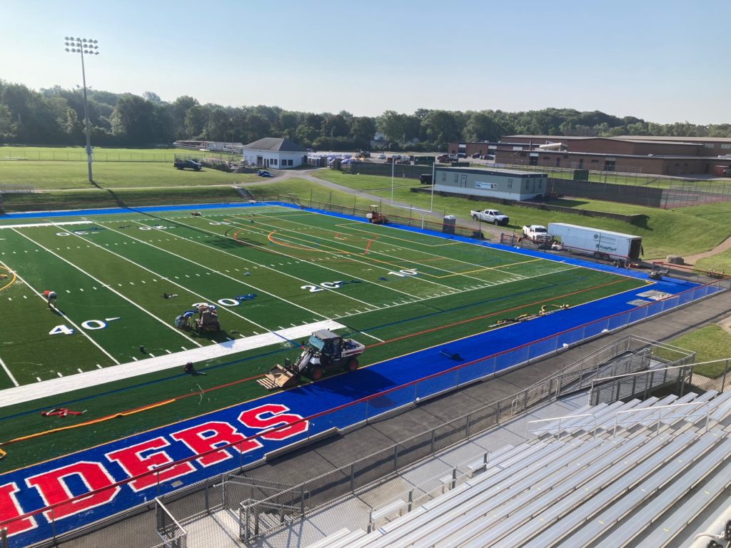 construction equipment on the sidelines of a stadium with new turf and lettering