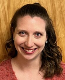 Photo of a woman with curly hair. She is smiling at the camera