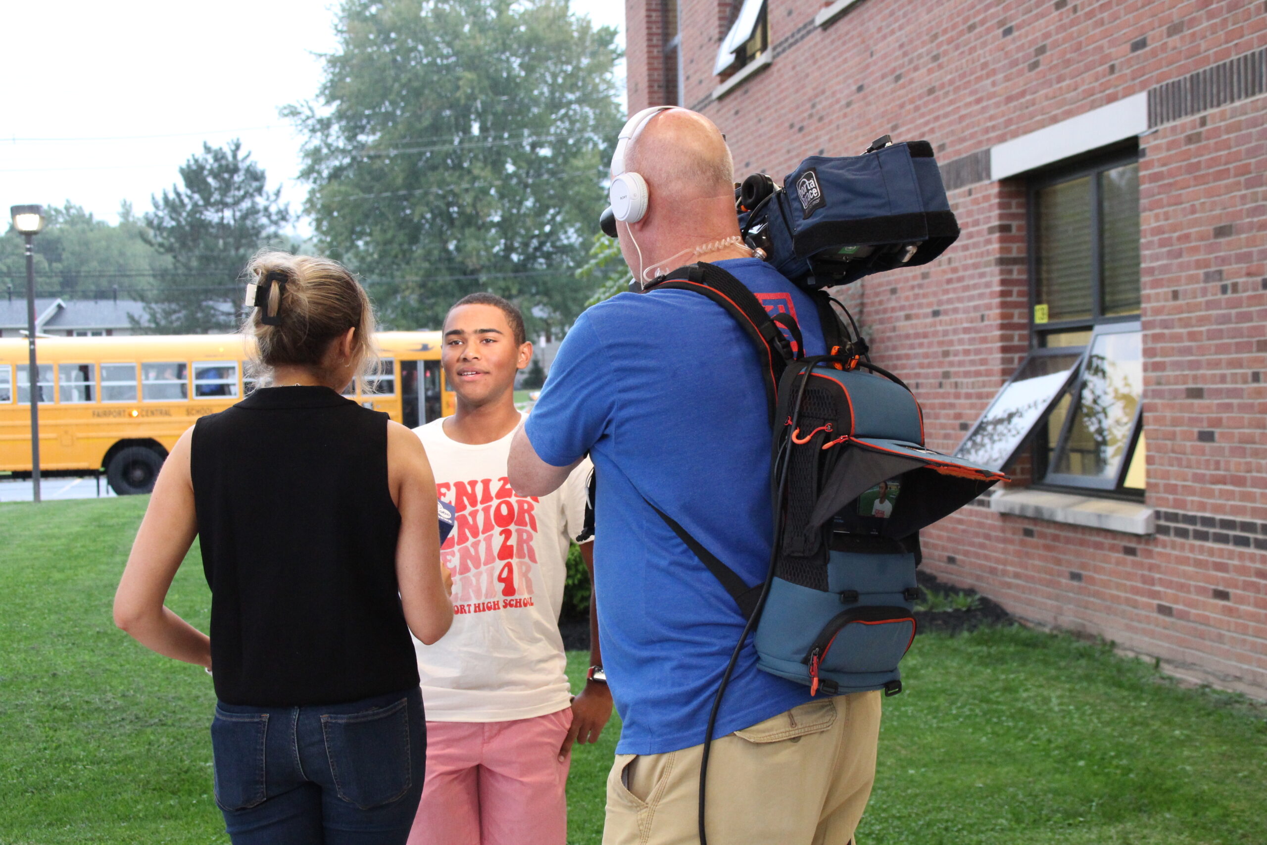 A reporter and a photographer for a news station interview a high school senior in front of a school