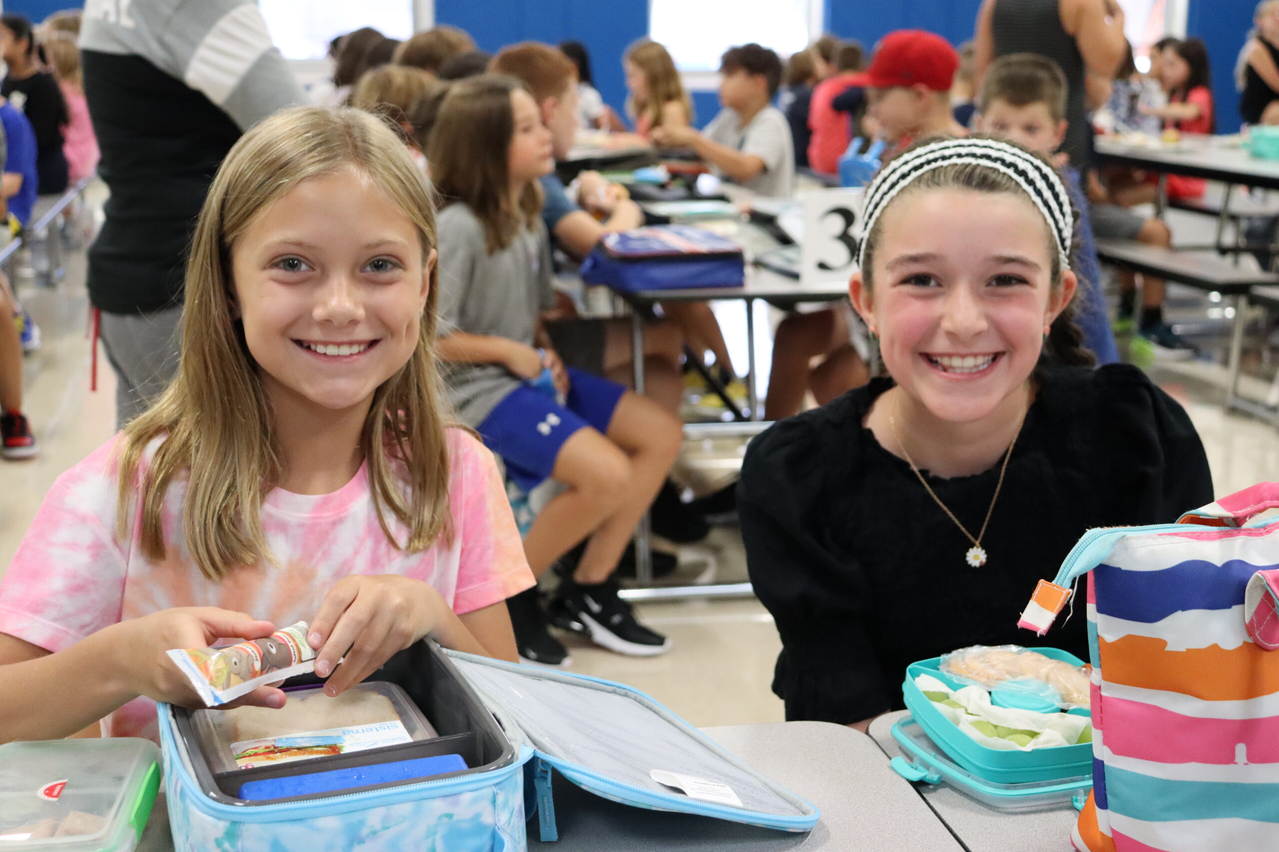 Two elementary school students smile at the camera behind open lunch boxes