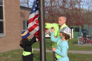 Two students and an adult lower the American flag