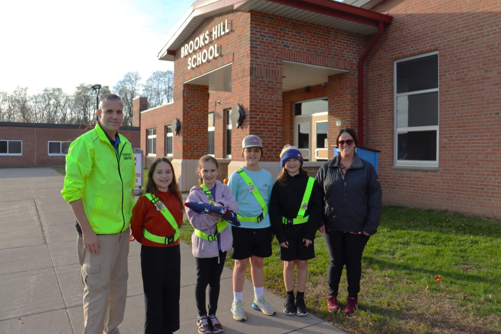 Two adults and four students stand in front of an elementary school.