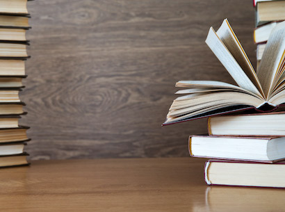 Books stacked on a wooden table and one book is fanned open