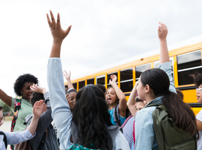  Students cheering outside in front of a school bus