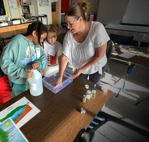 Glynn Middle School Eco-Club facilitator Katy Smith guides two young participants through a hands-on activity about pollution in coastal waters including oil spills and microplastics.