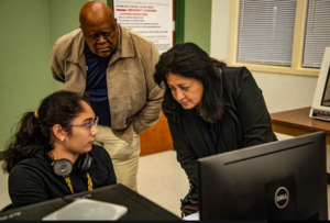 Tech educators Barry Harris, center, and Teresan Taw\'a, right, talk with GICCA student Kara Nuque who was working on a program to control traffic lights in a lab.