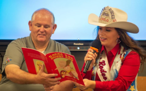 Jessie Lynn Nichols, Miss Rodeo USA, reads \"Rodeo Red\" to kindergarteners at Glyndale Elementary while Exchange Club Vice-Chairman Steven Floyd holds the book.