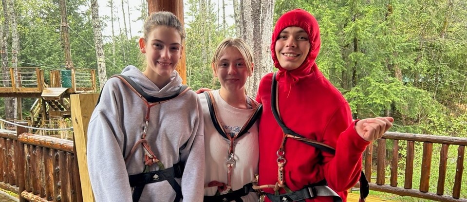 three students strapped in ziplining harnesses, smiling