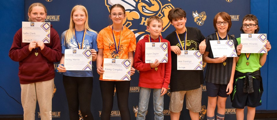 seven older students holding awards in front of hornet backdrop