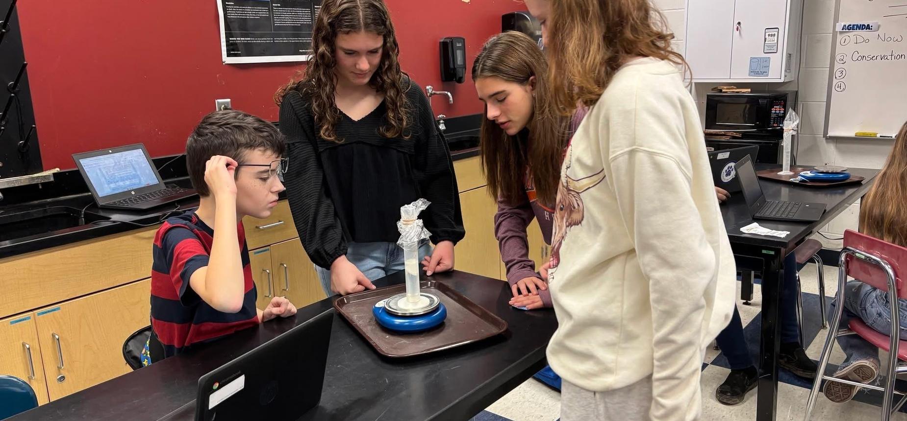4 students at a table looking at a graduated cylinder