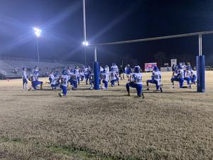 the image is of the HHS varsity football team in their blue and white uniforms, taking a knee under the goal post.