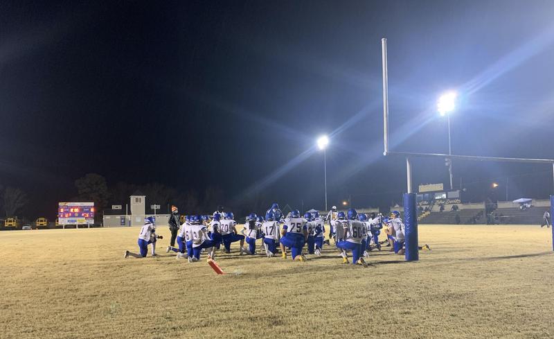 the image is of the 2021 varsity football team taking a knee at the end zone.