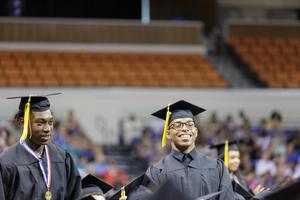 the image is of two black male high school seniors at graduation in their caps and gowns