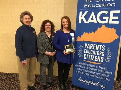 Three individuals with one holding a plaque next to a banner