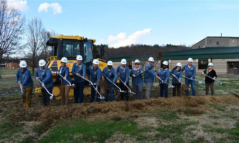  13 people holding shovels for groundbreaking in front of land mover