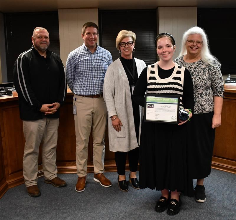 5 people, one holding a certificate, stand in front of desk