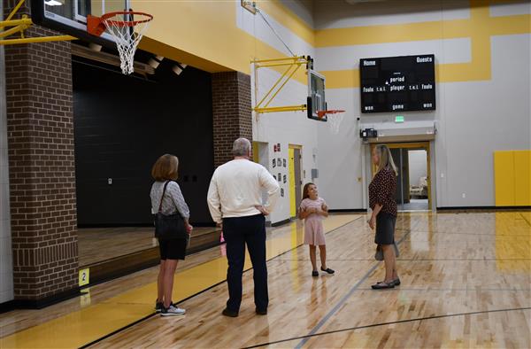 Four people stand talking in front of small stage in gym, next to basketball goals